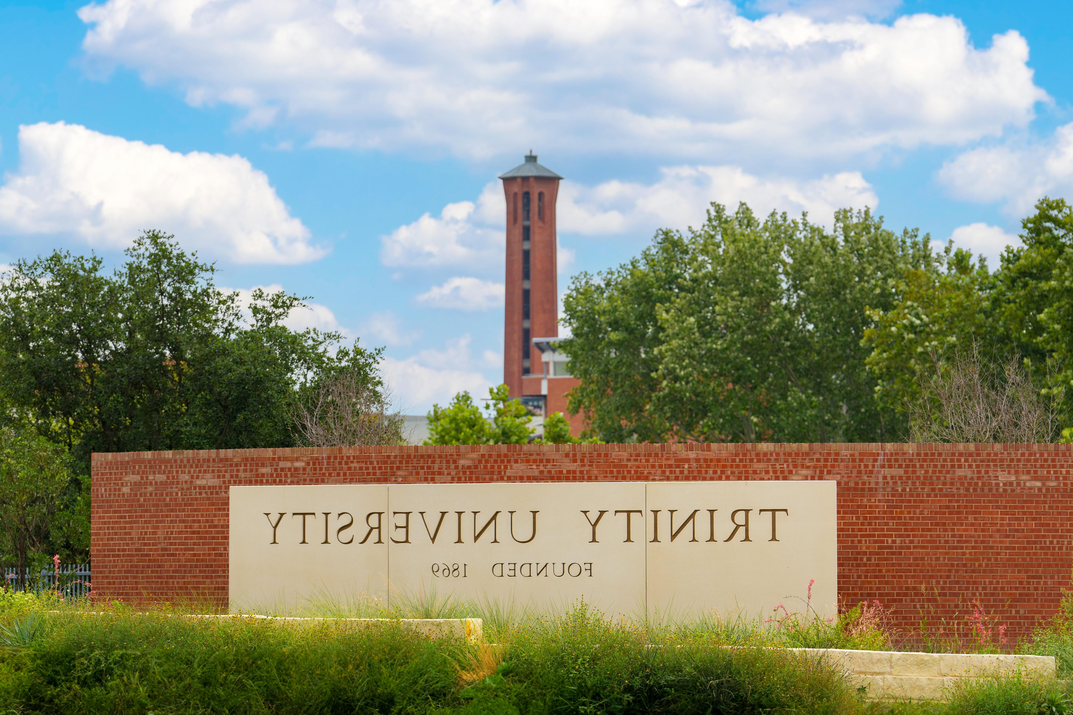 Trinity sign on a brick wall that reads Trinity University, Founded 1869.  Trinity Tower in the background