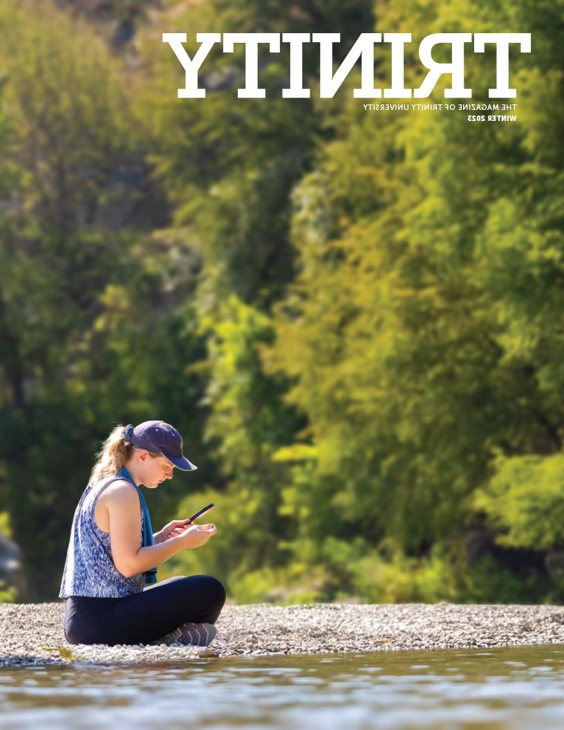 《2023年冬季三位一体》杂志的封面是一个人坐在靠近水的岩石上，通过放大镜观看