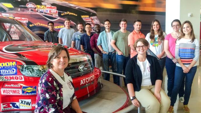 Picture of an accounting class standing in front of Toyota cars. 