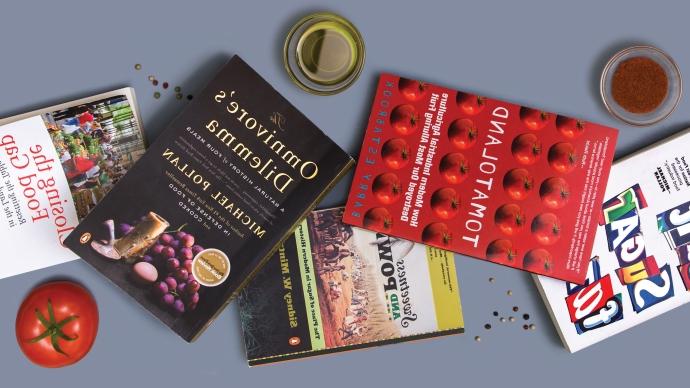 a curated stack of food-related books with spices and a tomato