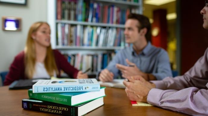 two students and ed schumacher sit around a table talking, with three health care textbooks on the table