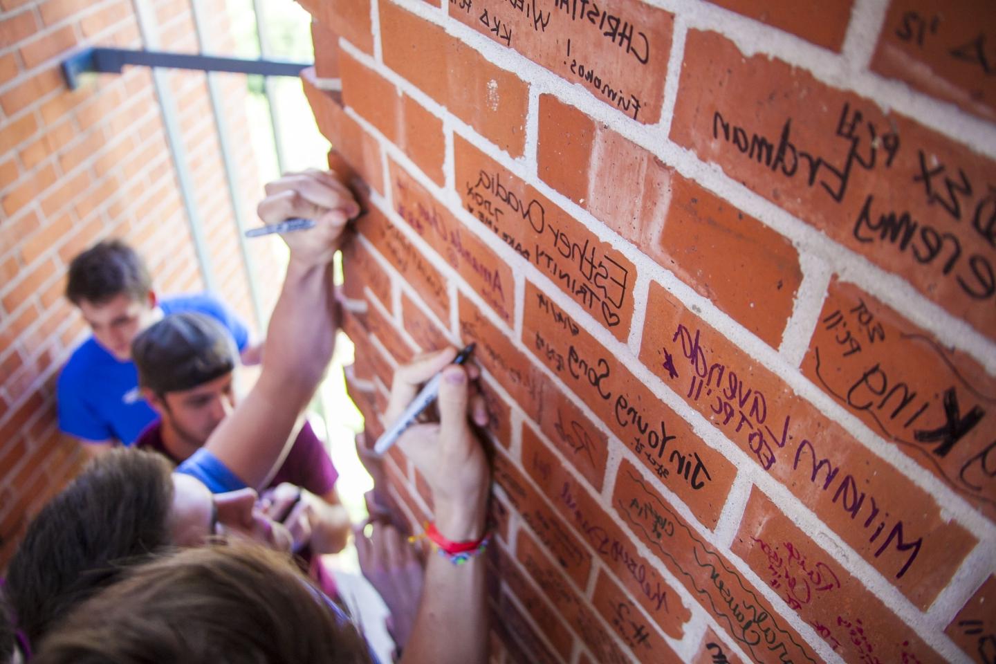 an overhead shot shows three students signing bricks inside murchison tower