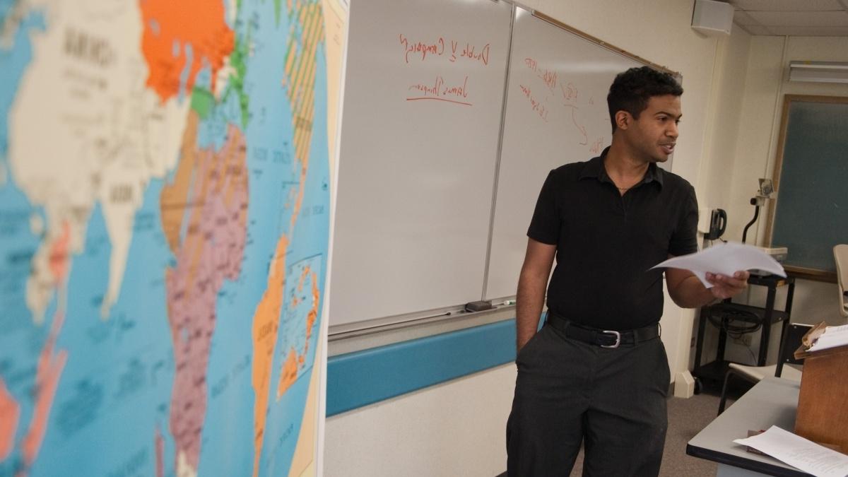 Professor teaching next to whiteboard and map of the world