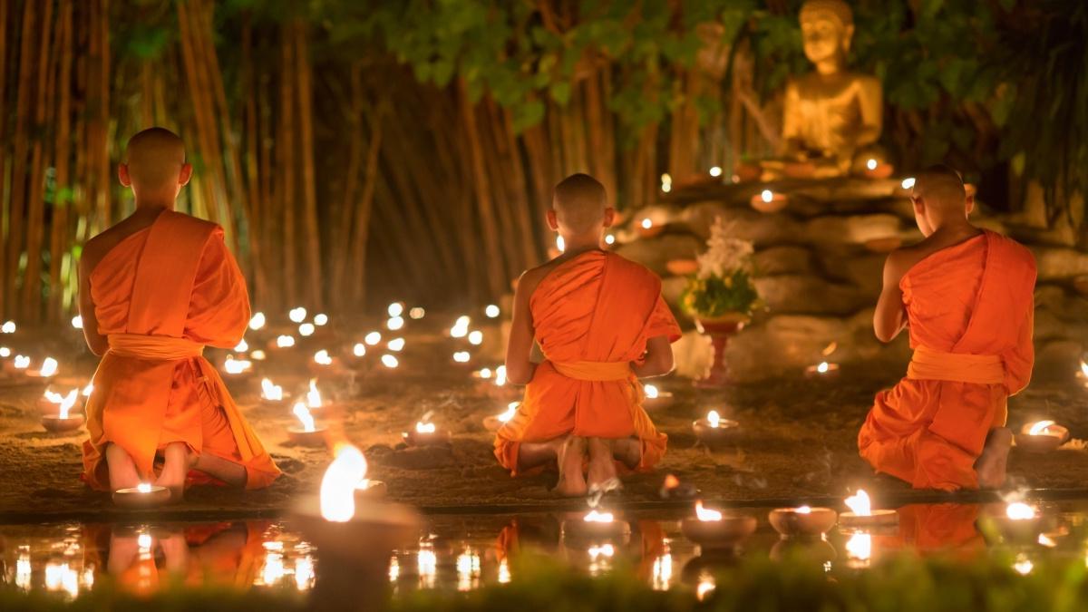 佛教徒在黑暗中跪着，周围是蜡烛，背景是佛像