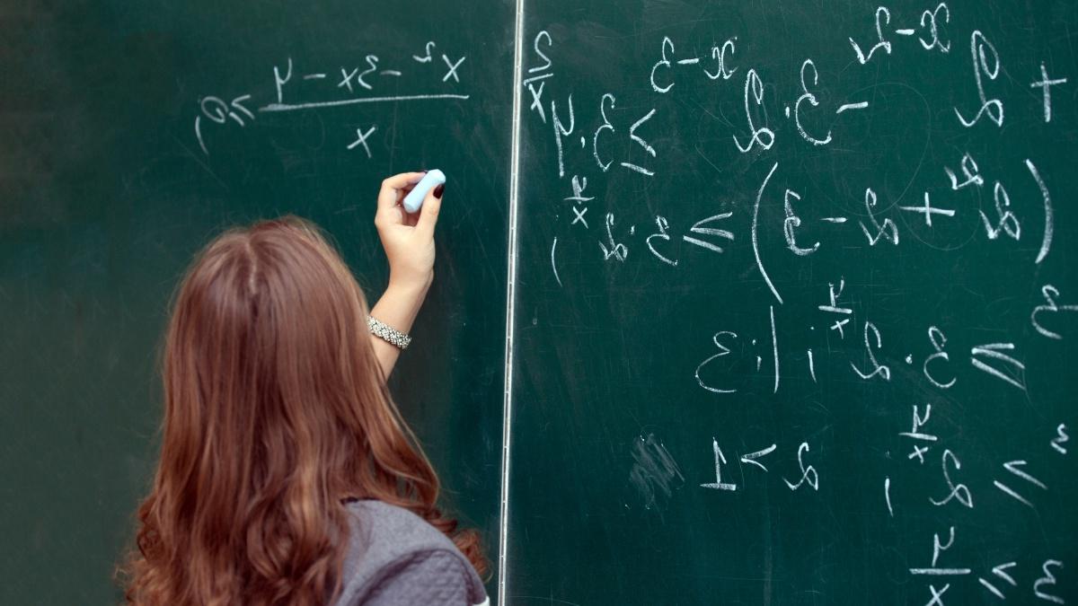 Female student solves a math problem on a chalkboard.
